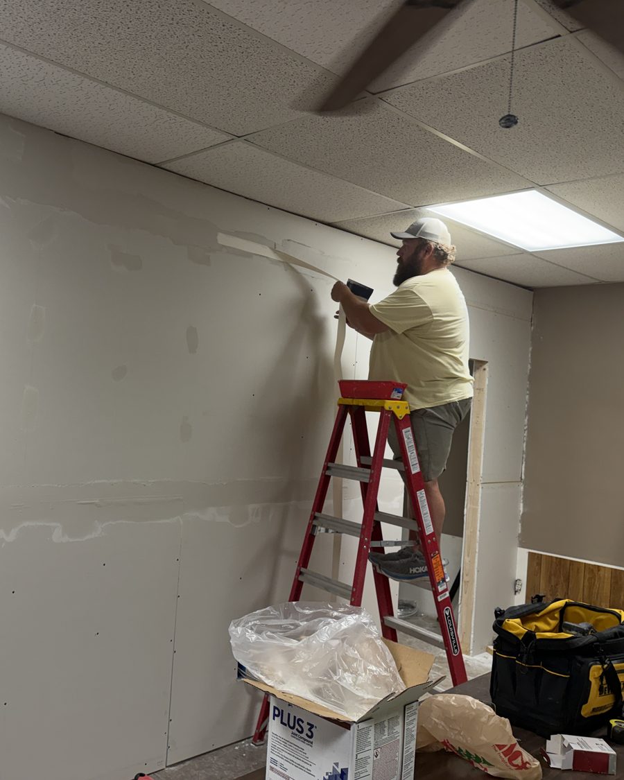 Zach Jeffery on a ladder, taping drywall to build out a new office at city hall
